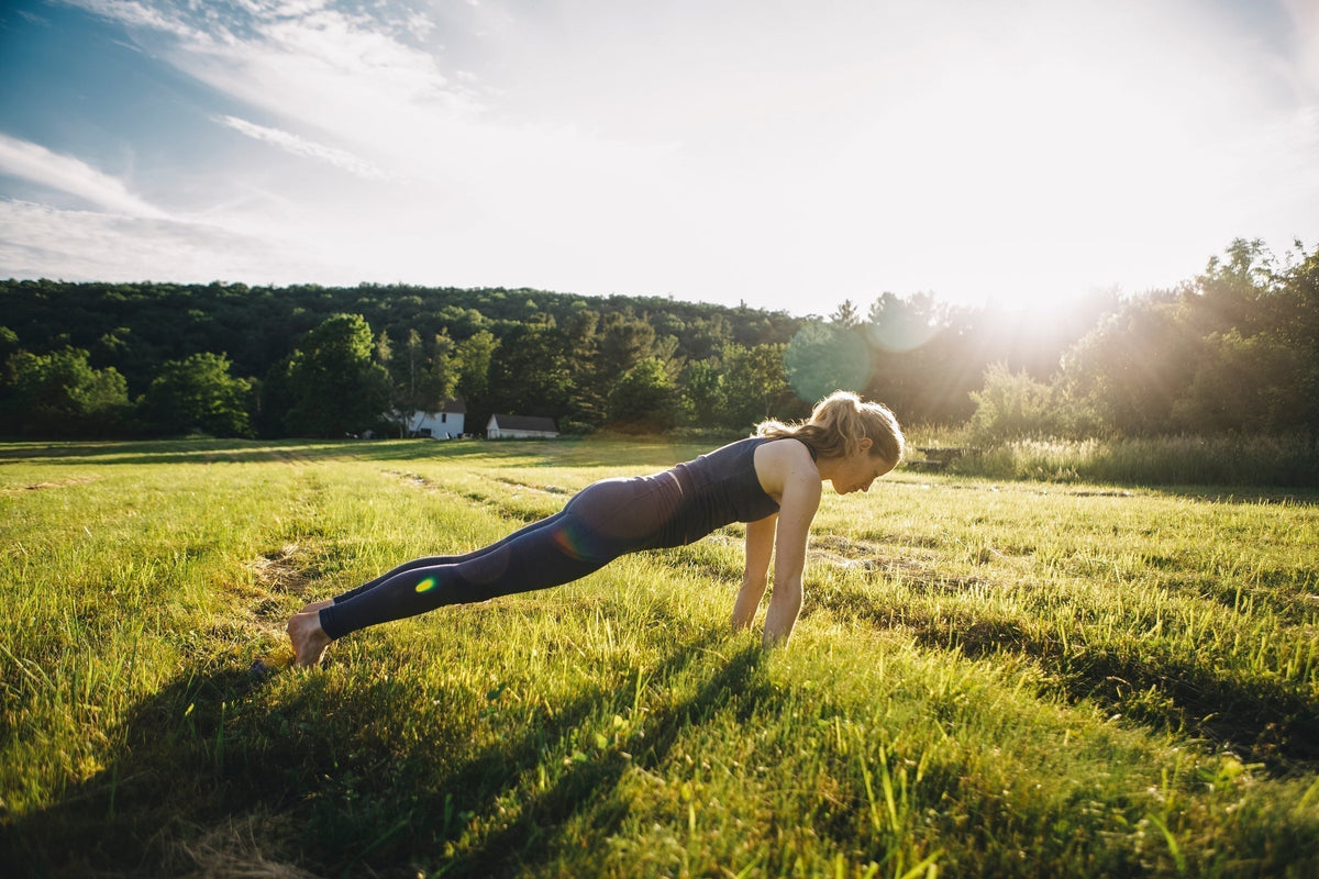 Junge Frau macht Liegestütze in einem Feld bei Sonnenschein