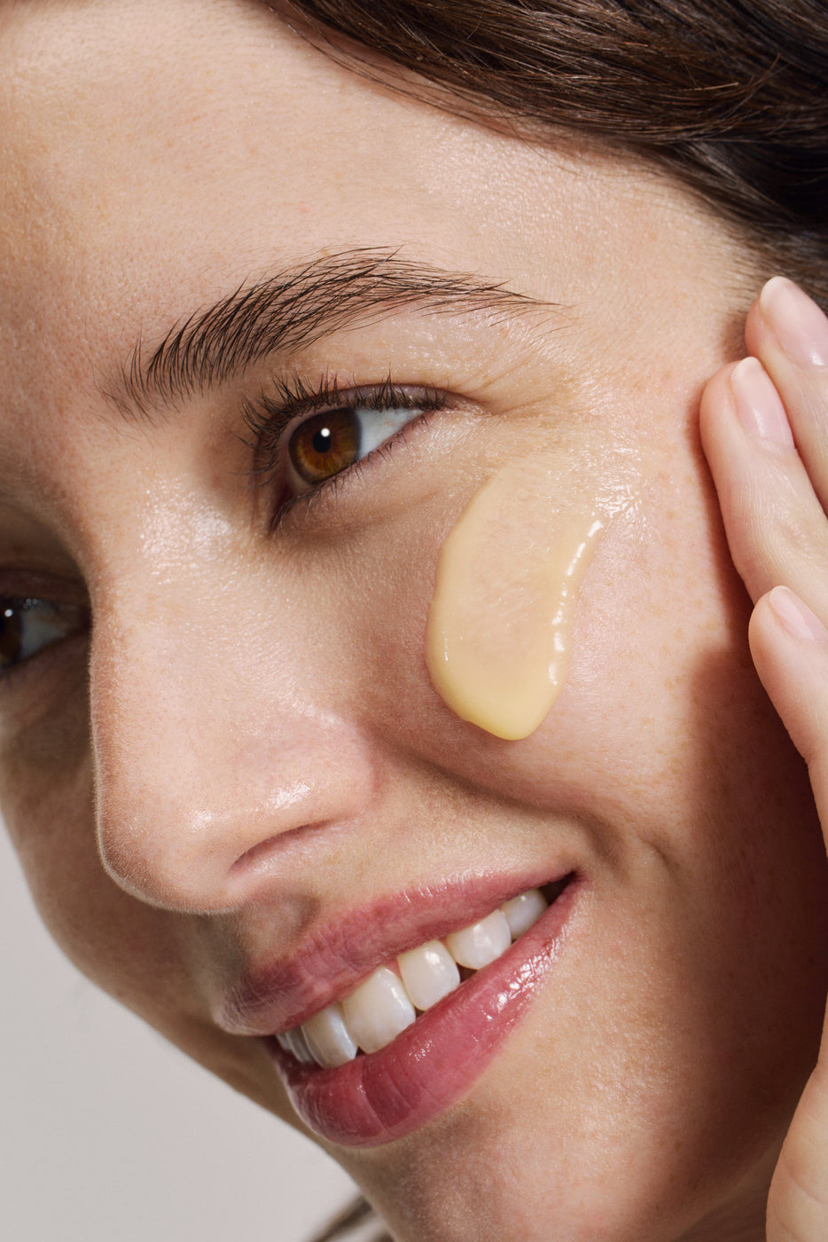 Nahaufnahme einer lächelnden Frau mit goldener Creme unterhalb des Auges