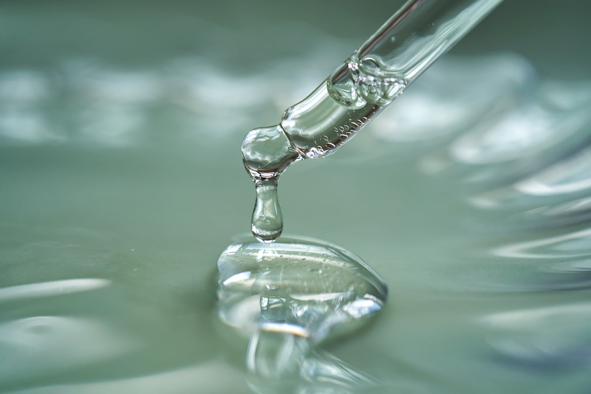 Pipette tropft klares Serum auf glänzende Geloberfläche, Makroaufnahme