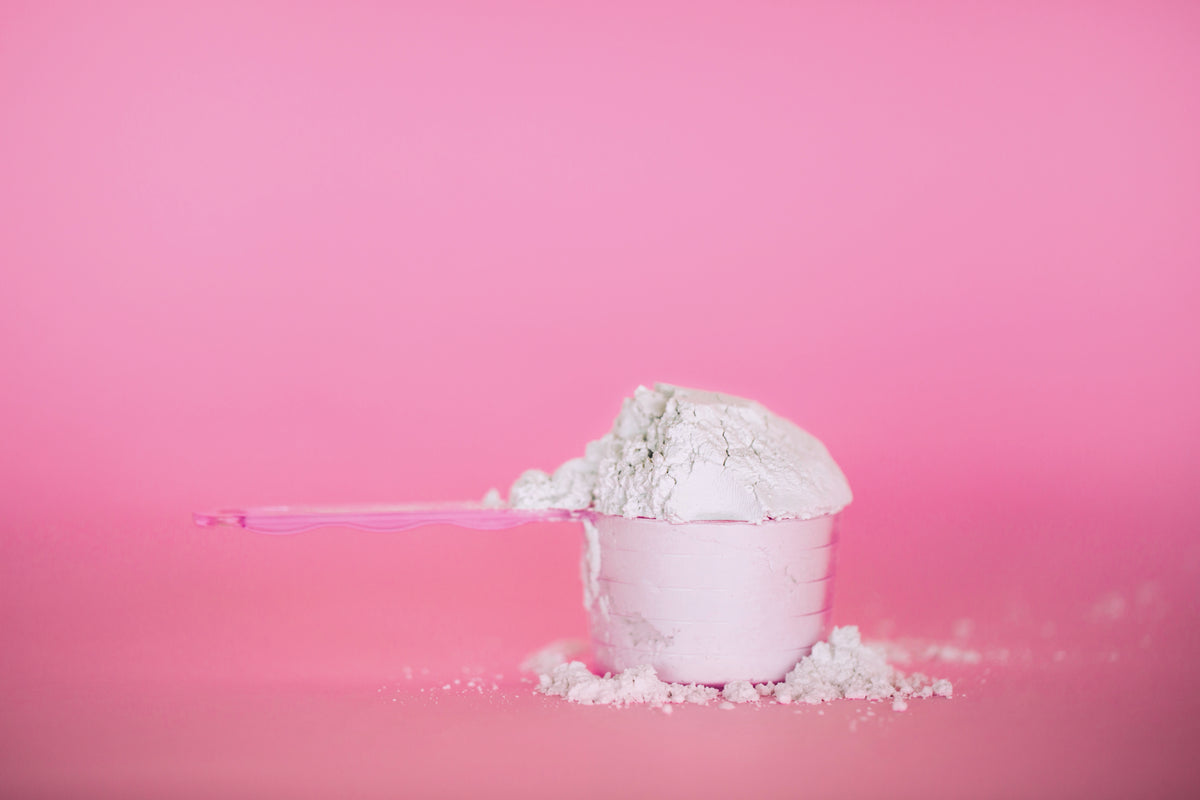 Messbecher mit weißem Pulver vor einem pinken Hintergrund