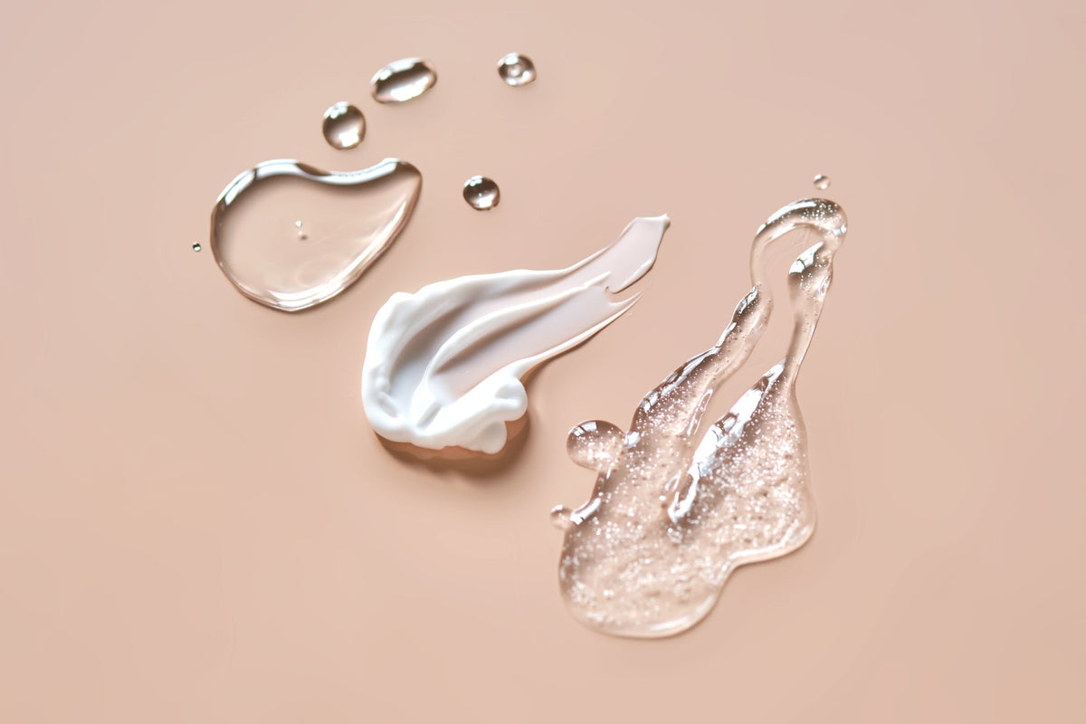 Texturen: weiße Creme, glitzerndes Gel und klare Tropfen auf beigem Hintergrund