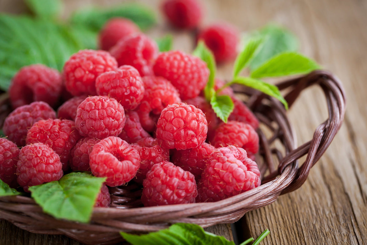 Korb voller Himbeeren mit grünen Blättern auf Holzuntergrund