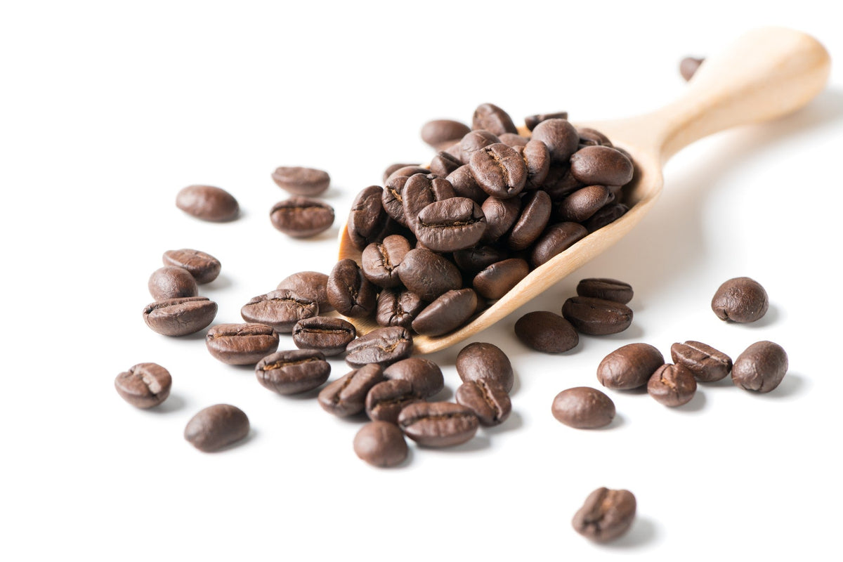 Braune geröstete Kaffeebohnen in einem Holzlöffel, einige Bohnen verstreut auf weißem Hintergrund.