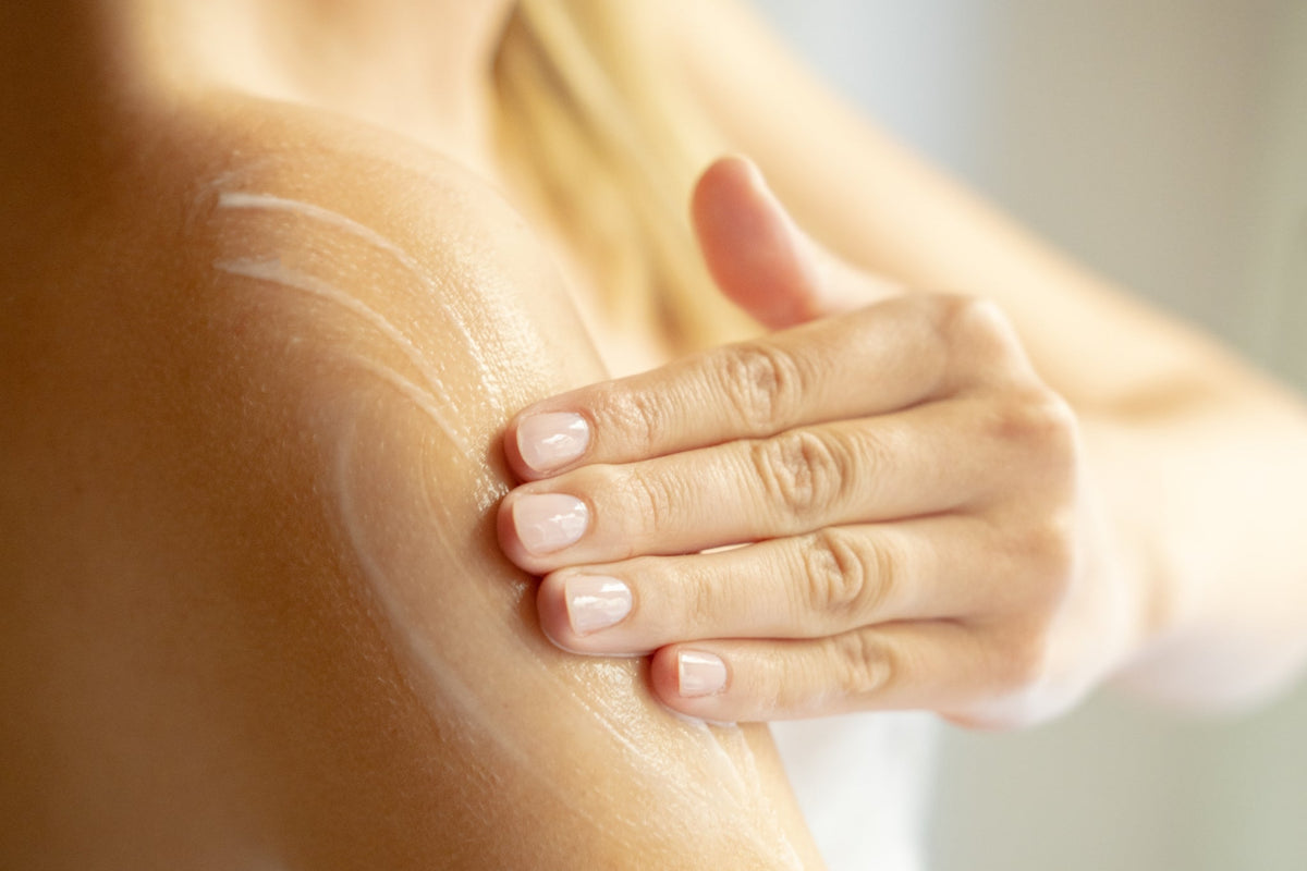 Hand trägt Creme auf nackte Schulter auf, Nahaufnahme.