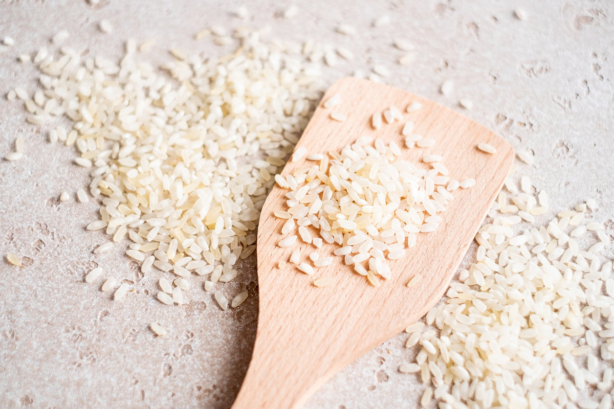 Holzlöffel mit weißen Reiskörnern, auf einem Tisch verstreut