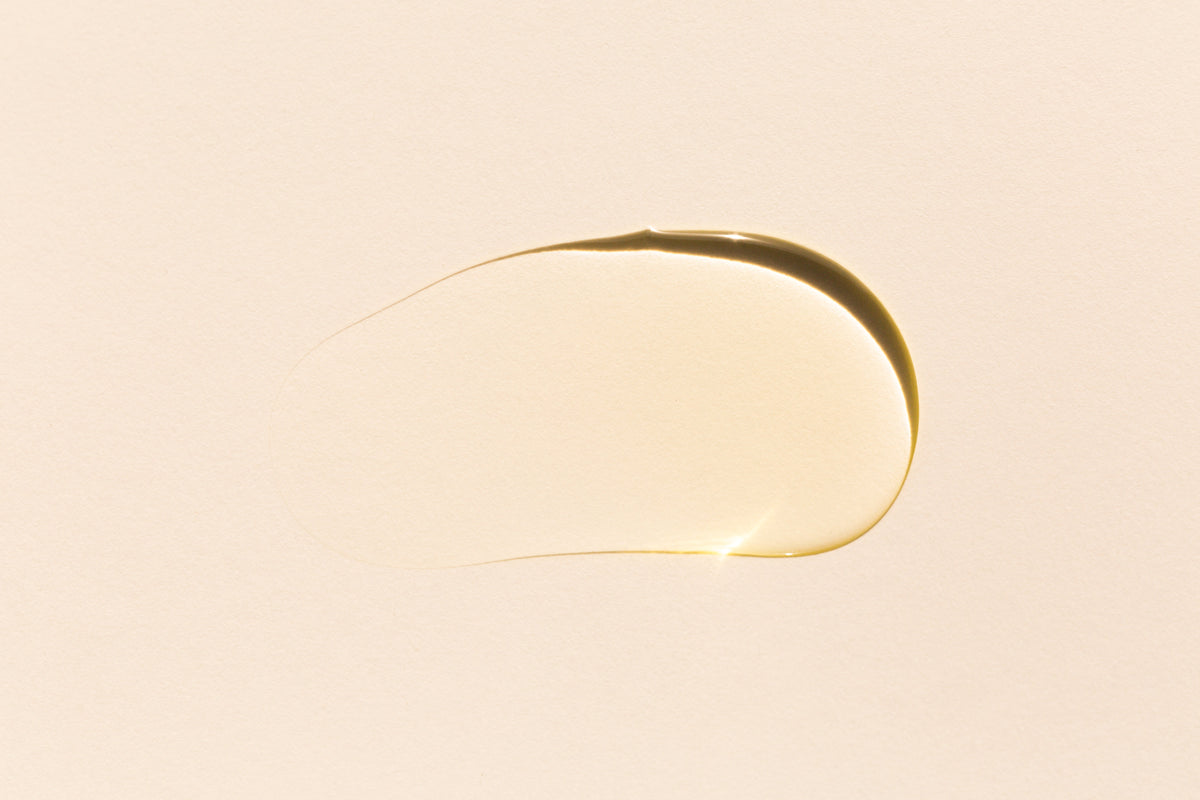 Nahaufnahme eines goldenen Tropfens Flüssigkeit auf hellem Hintergrund, Symbol für pflegende Wirkstoffe wie Peptide.